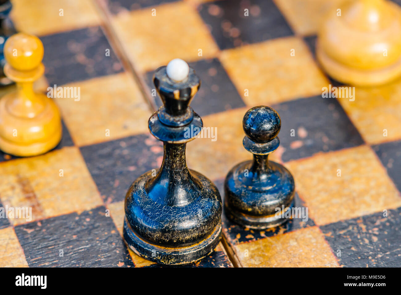 Viejo y usado, soportó la Reina negra de ajedrez y un peón en un tablero de  ajedrez. Se centran en un peón, Peón blanco de ajedrez es visible  Fotografía de stock -