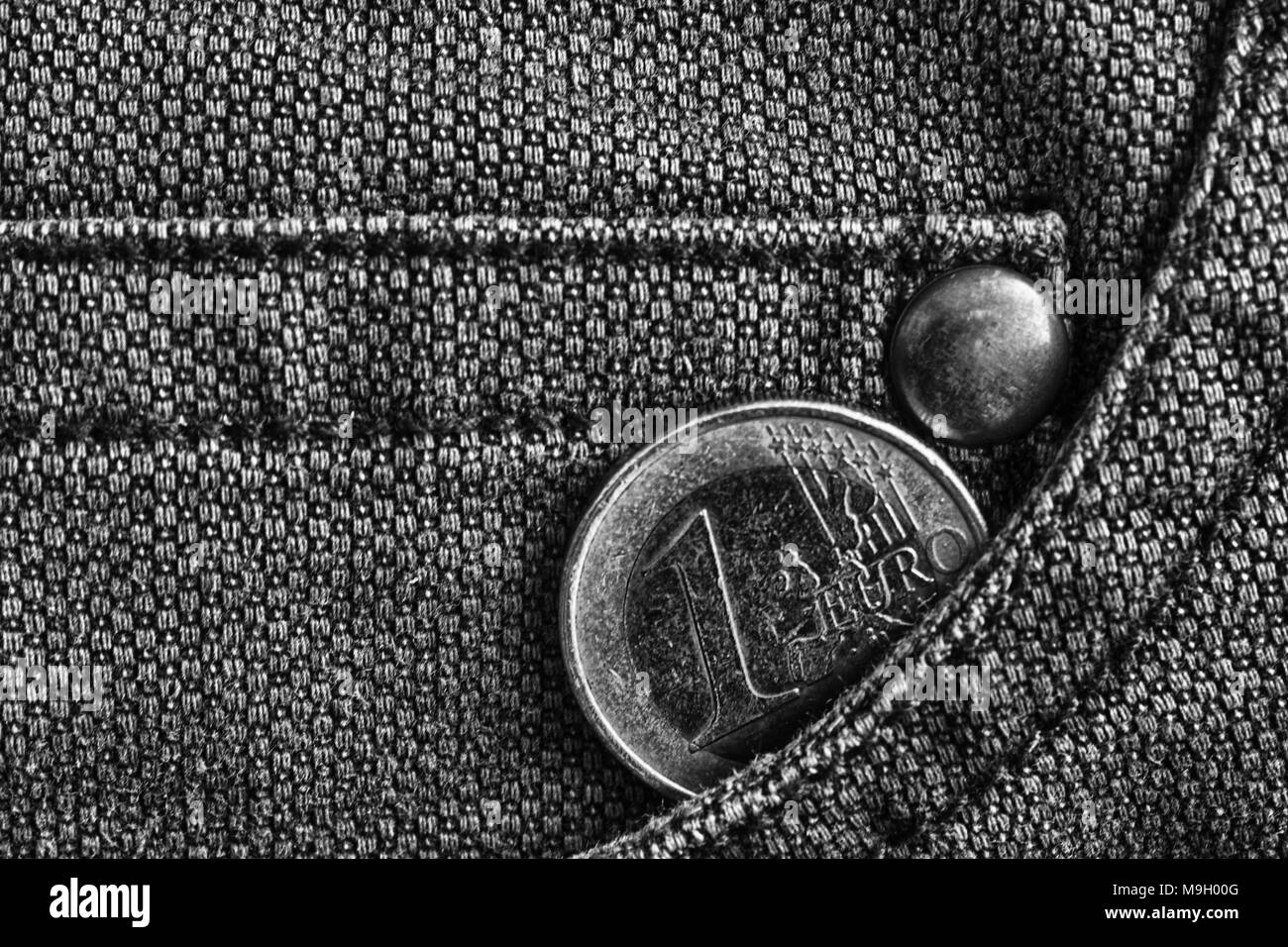 Monedas de euro con una denominación de un euro en el bolsillo de los pantalones vaqueros desgastados, captura monocromo. Foto de stock