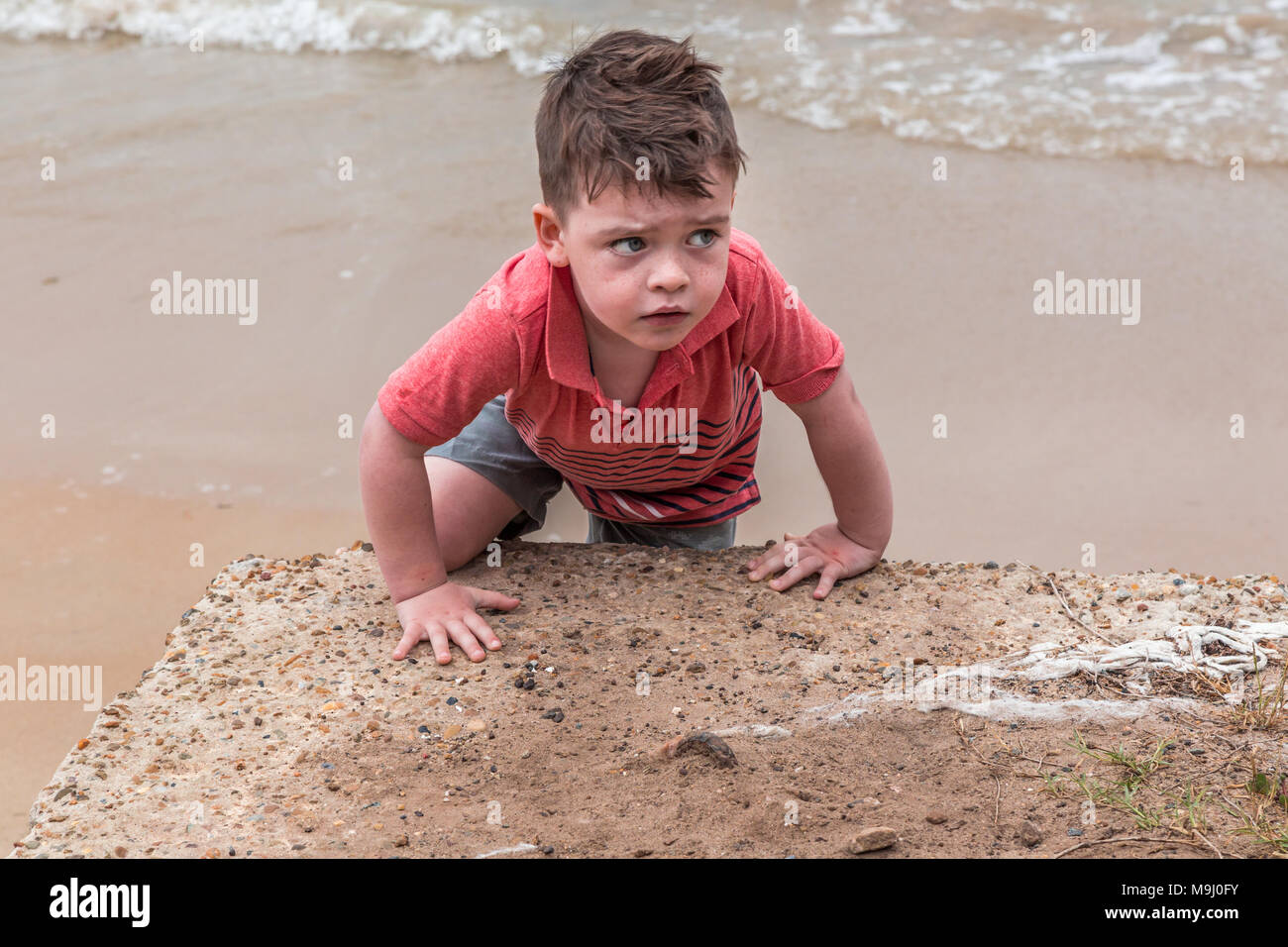 Ansioso buscando pequeño niño, escalada sobre una roca en el mar. Foto de stock