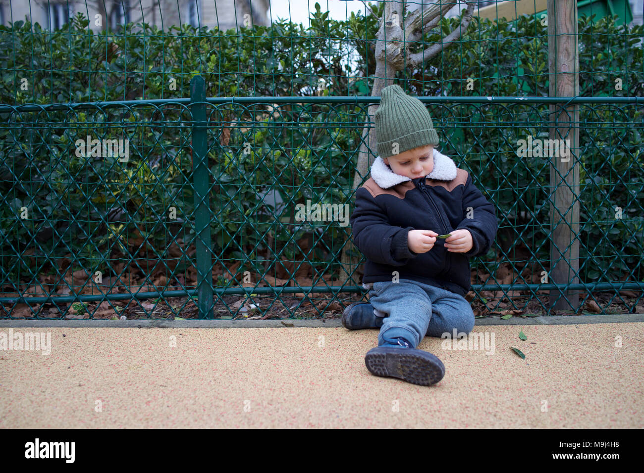 Muchacho sentado en el piso, solo en el patio de recreo, buscando vulnerables Foto de stock