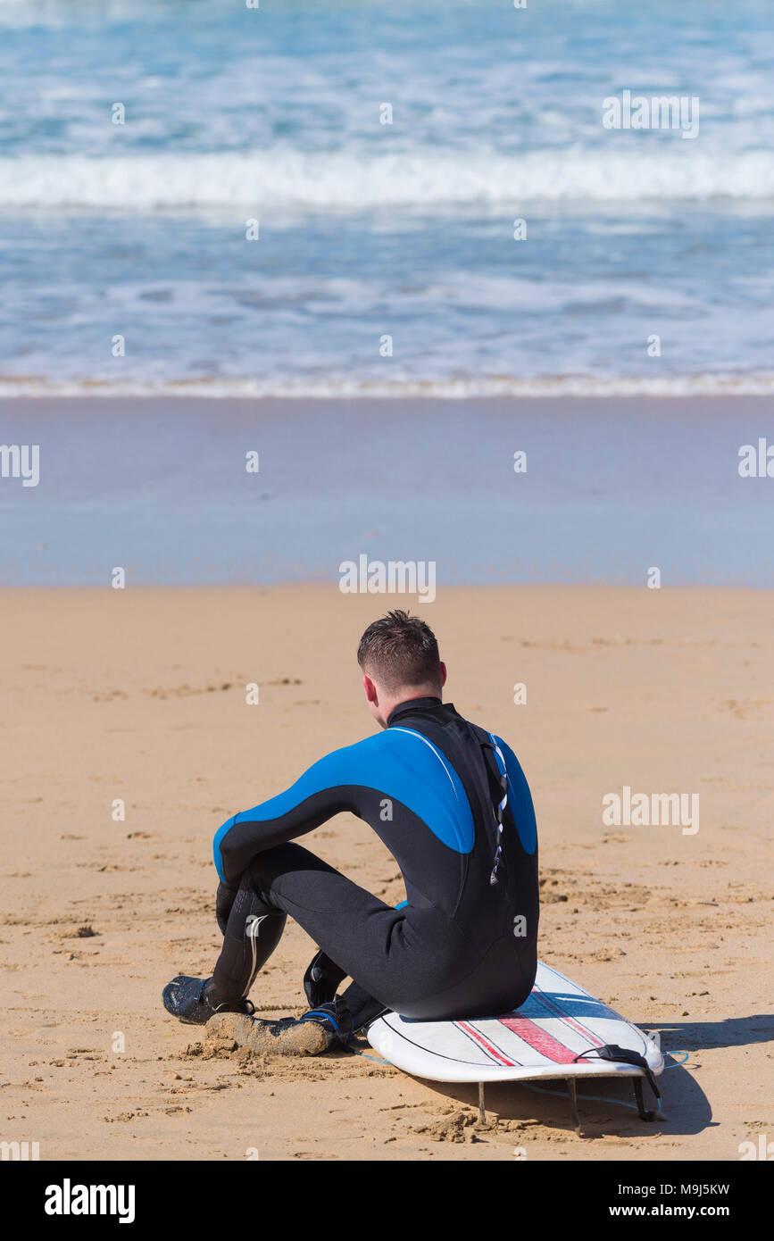 Reino Unido el surf - un surfista sentarse a descansar en su tabla de surf en la playa Fistral en Newquay Cornwall Foto de stock