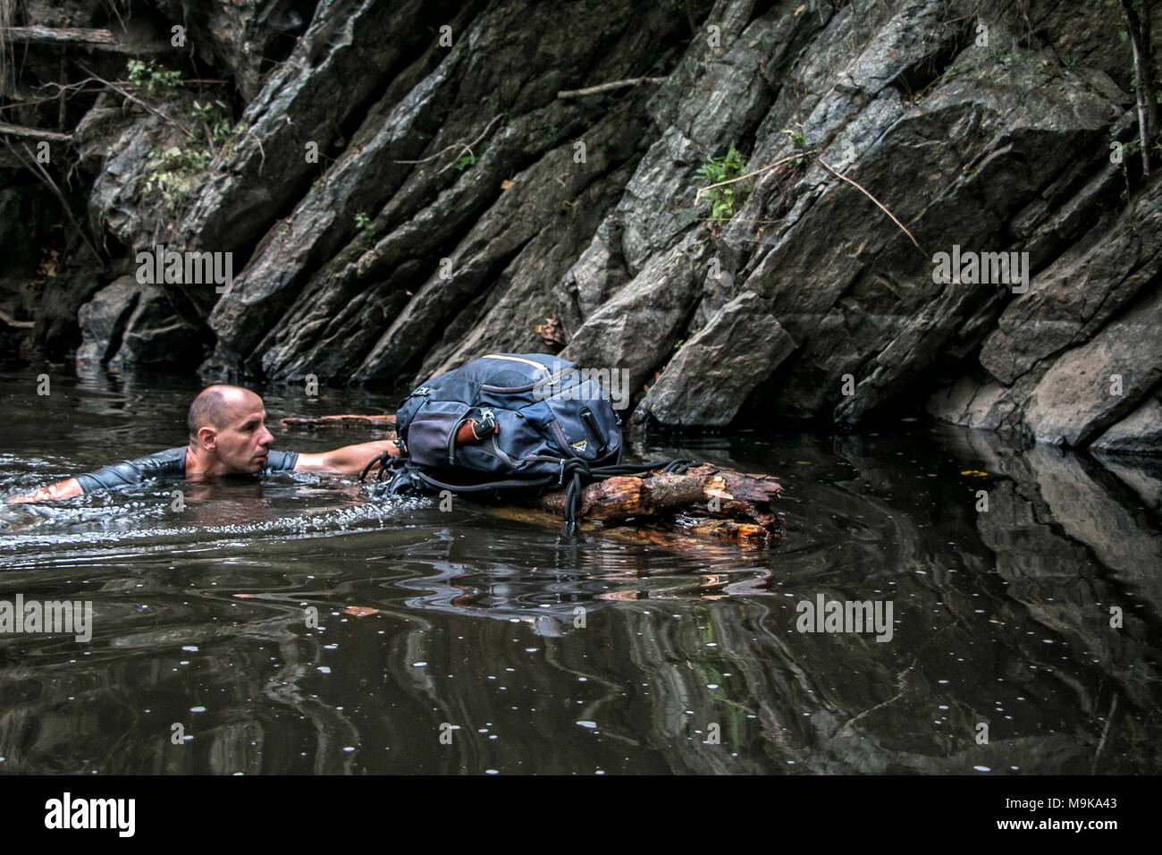 Un hombre es nadar en un río y apoyar una balsa improvisada hecha a mano con su mochila. Concepto de la supervivencia y la exploración en el desierto Foto de stock