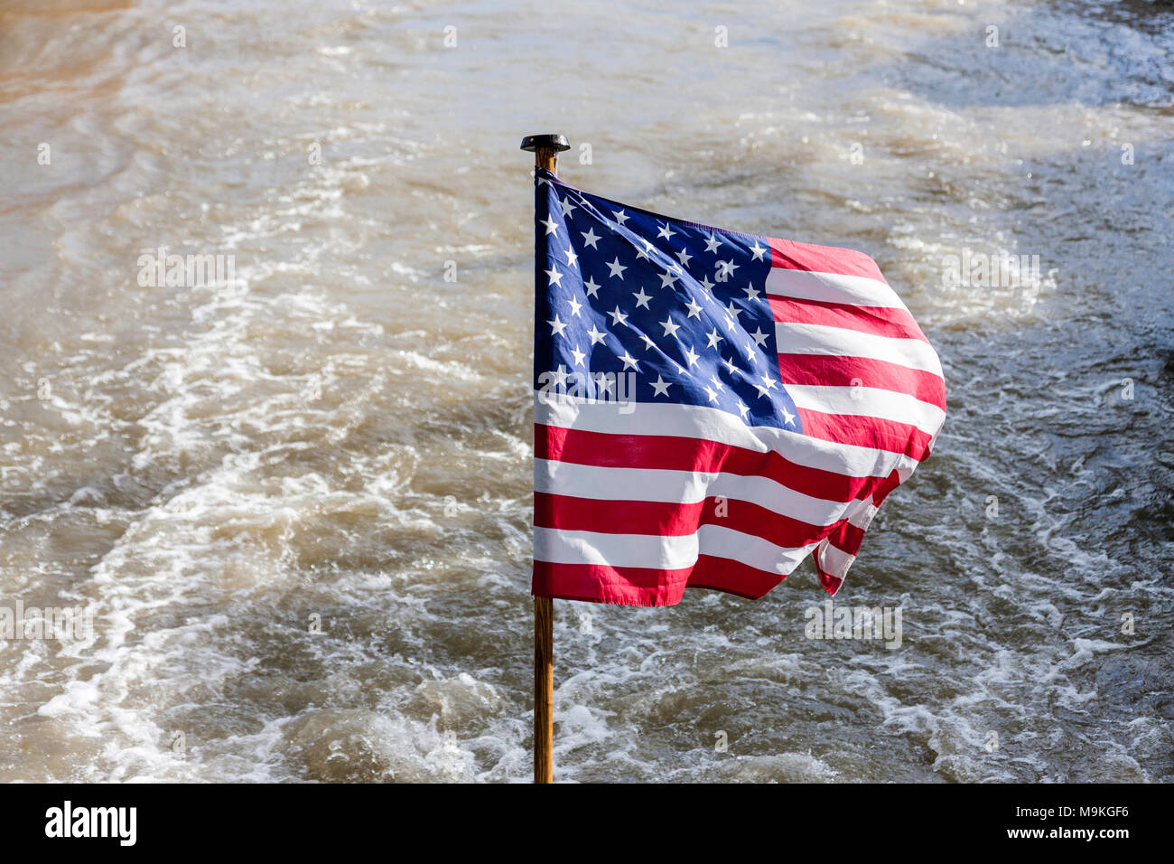 Estados Unidos de América soleada bandera ondea en la brisa contra el fondo de la estela de un río en bote a motor. Foto de stock
