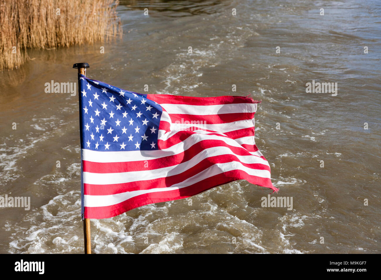 Estados Unidos de América soleada bandera ondea en la brisa contra el fondo de la estela de un río en bote a motor. Foto de stock