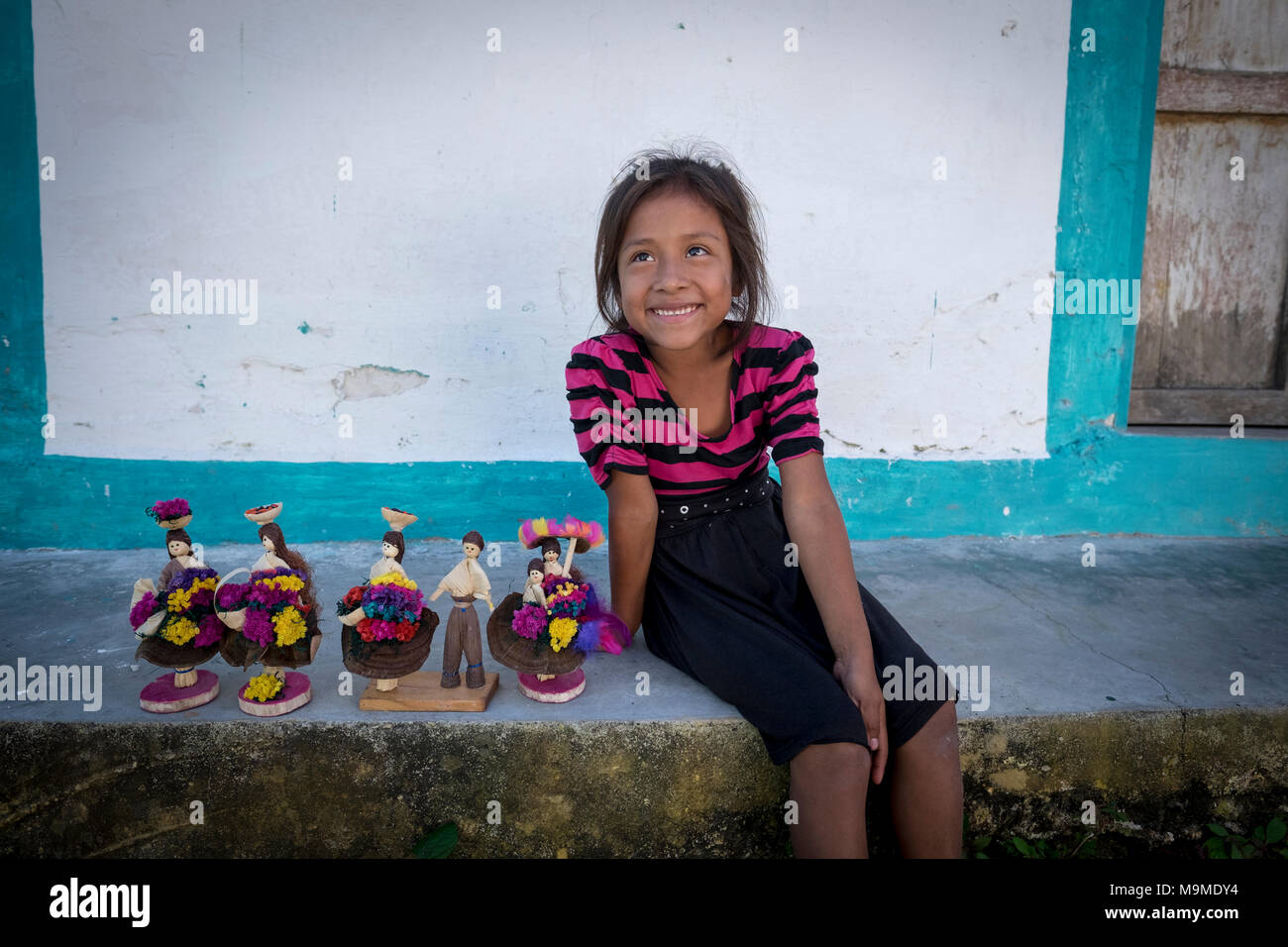 Joven Niña maya sonríe mientras vende sus muñecas sobre los pasos de su homel en Guatemala Foto de stock