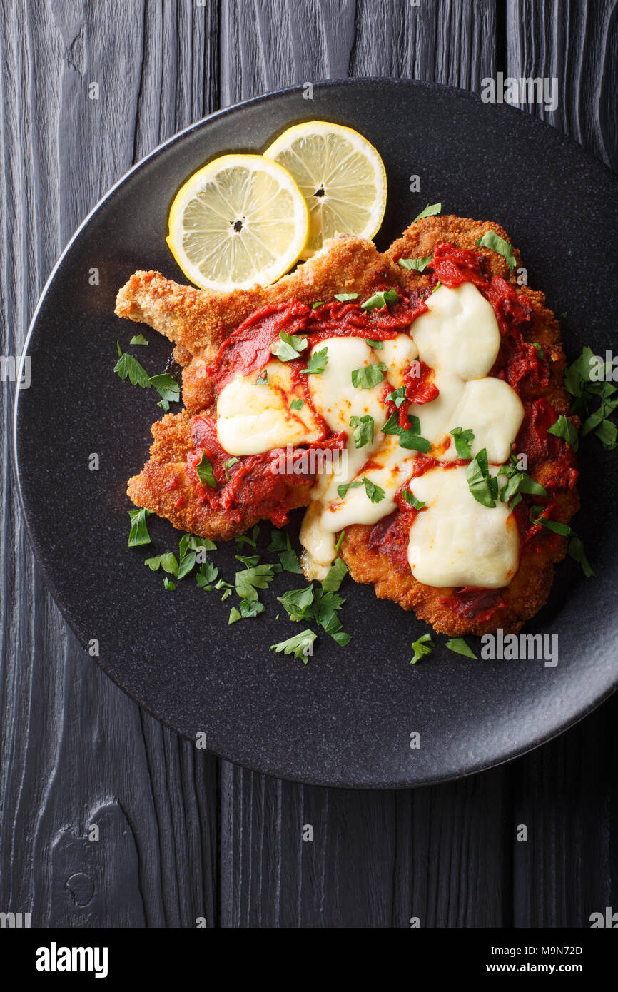 La milanesa napolitana - chuleta de ternera casero con queso mozzarella, limón y salsa de tomate de cerca en una placa. Vista superior de la vertical desde arriba Foto de stock