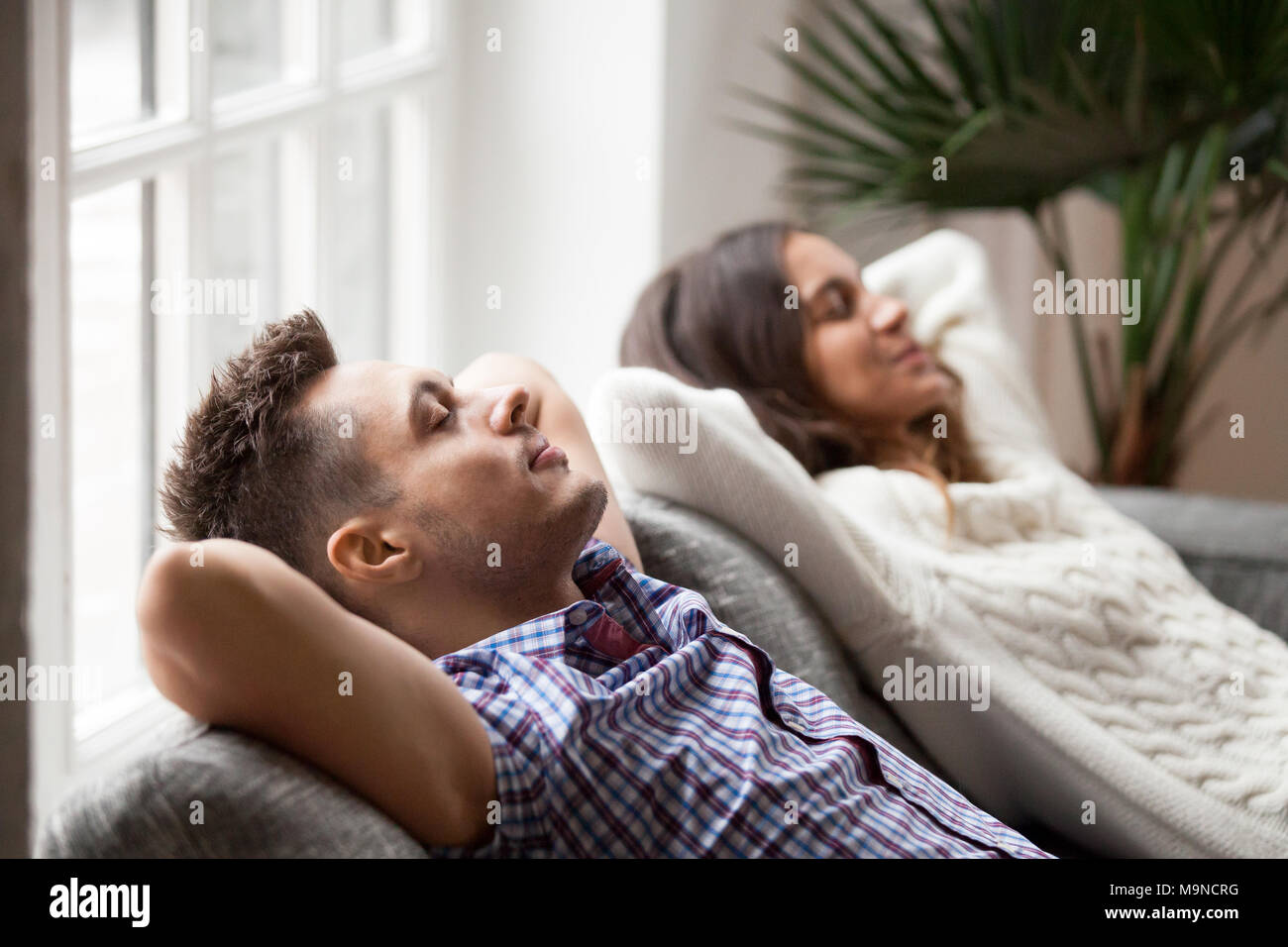 Pareja joven descansando en un cómodo sofá en casa juntos, feliz al hombre y a la mujer disfrutar de la relajación o nap dormitando en el sofá con los ojos cerrados, calma famil Foto de stock