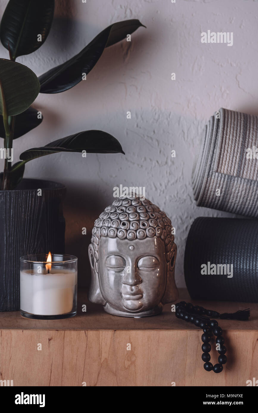 Escultura de cabeza buda, velas encendidas y colchonetas para yoga en  estante de madera Fotografía de stock - Alamy