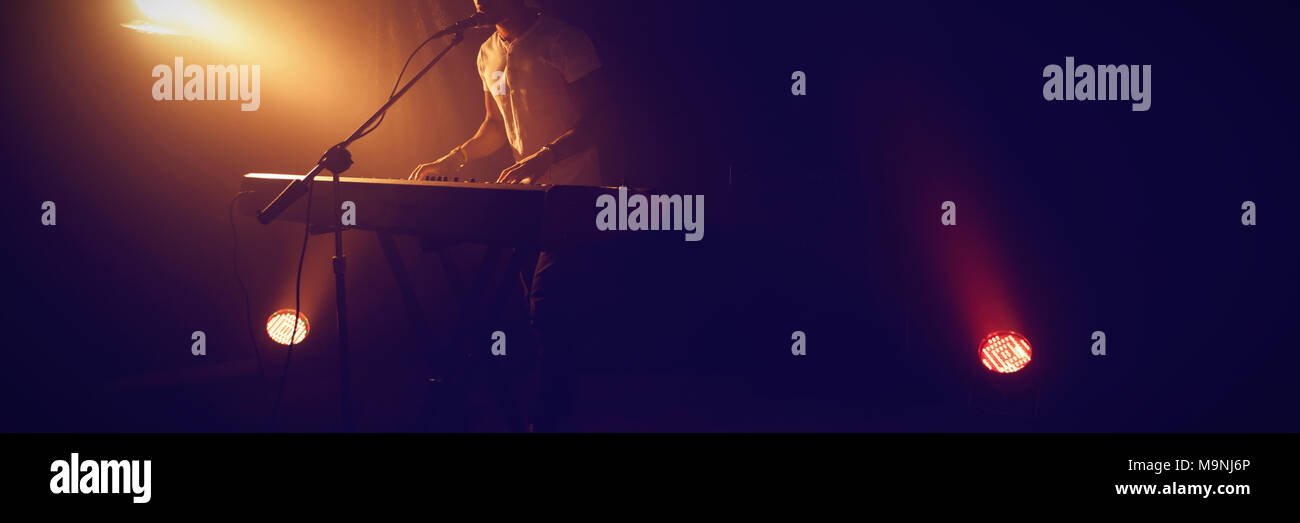 Hombre cantando mientras toca el piano en el club iluminada Foto de stock
