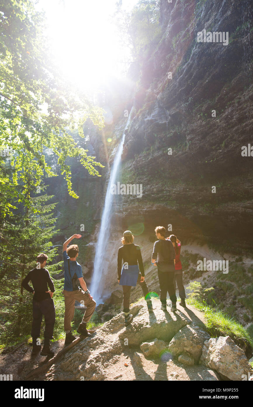 Grupo de jóvenes de pie al pie de la cascada en Pericnik Vrata valle cerca de Mojstrana alpino en el Parque Nacional de Triglav, en Eslovenia Foto de stock