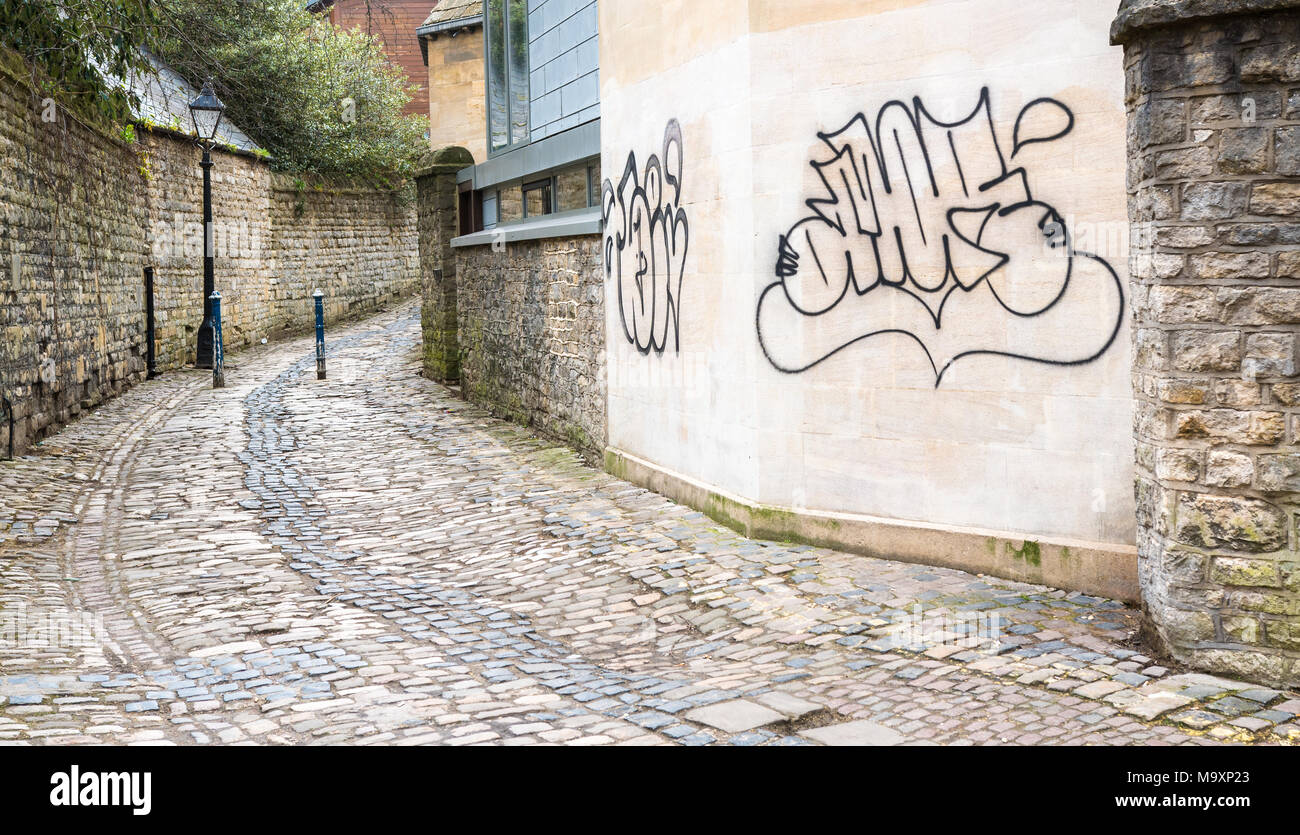 Graffitii en una pared exterior (junto a una calle adoquinada) de la universidad de la Nuffield College en la ciudad de Oxford, Inglaterra. Foto de stock