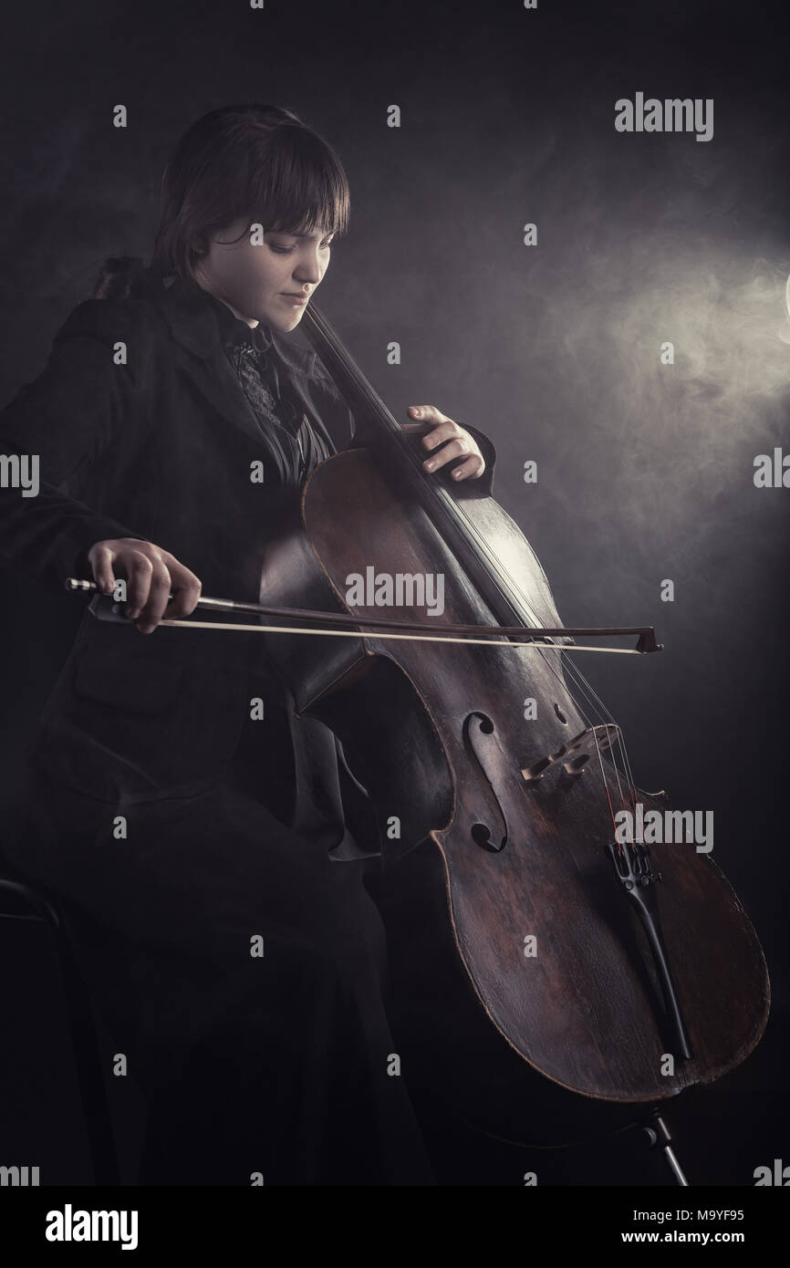 La violonchelista tocando música clásica en el cello contra un fondo negro. Niebla en el fondo. Foto de Estudio Foto de stock