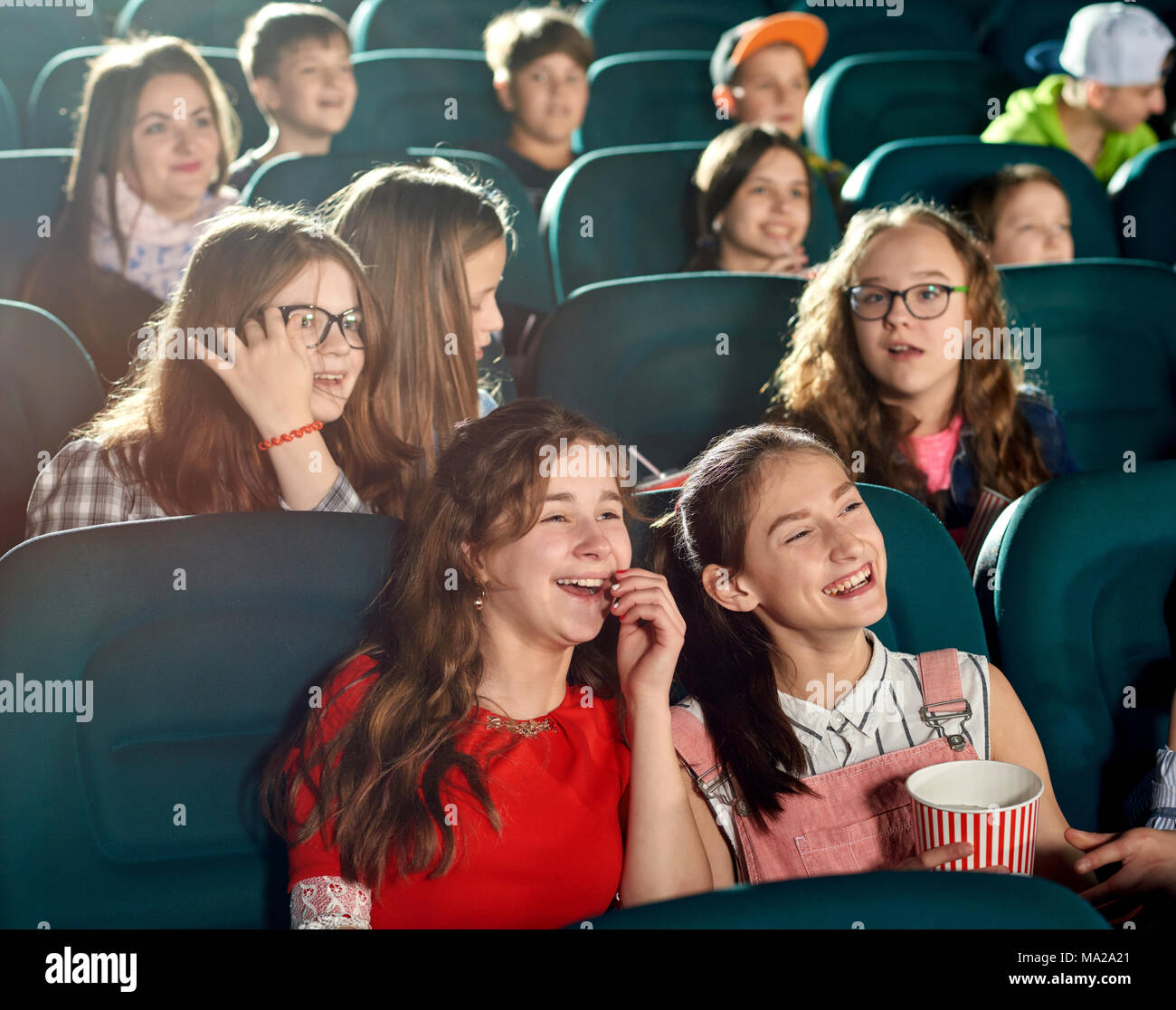 Feliz niñas riendo viendo interesante película en el cine. Ellos sonriendo, mirando satisfechos. Hay muchos otros niños emocional en el fondo. Foto de stock