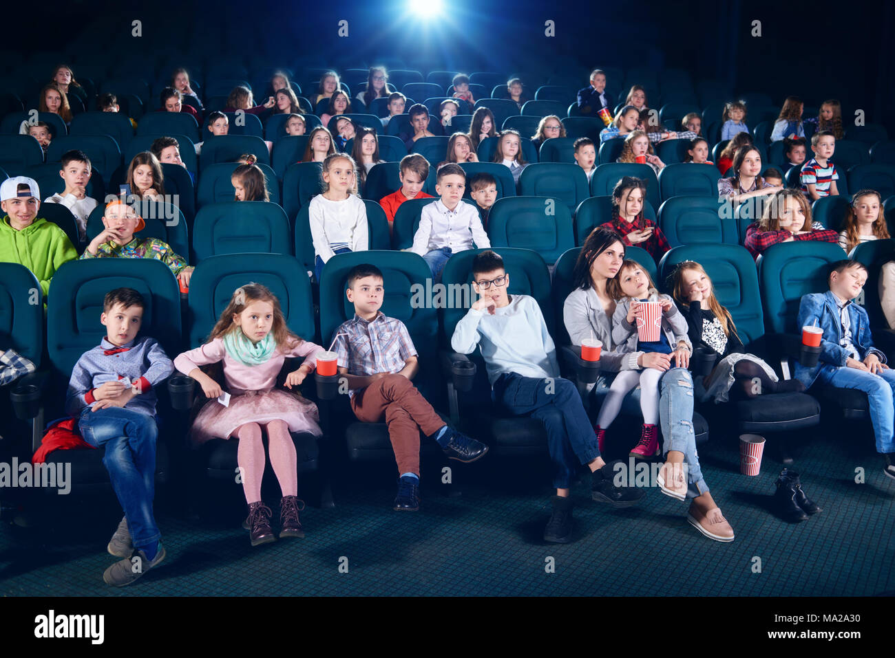 Frontview de gente sentada en la sala de cine. Los niños y las niñas viendo la película interesante y mirando muy emocional, asustado y salió. Los niños portan coloridos ropa de moda. Foto de stock