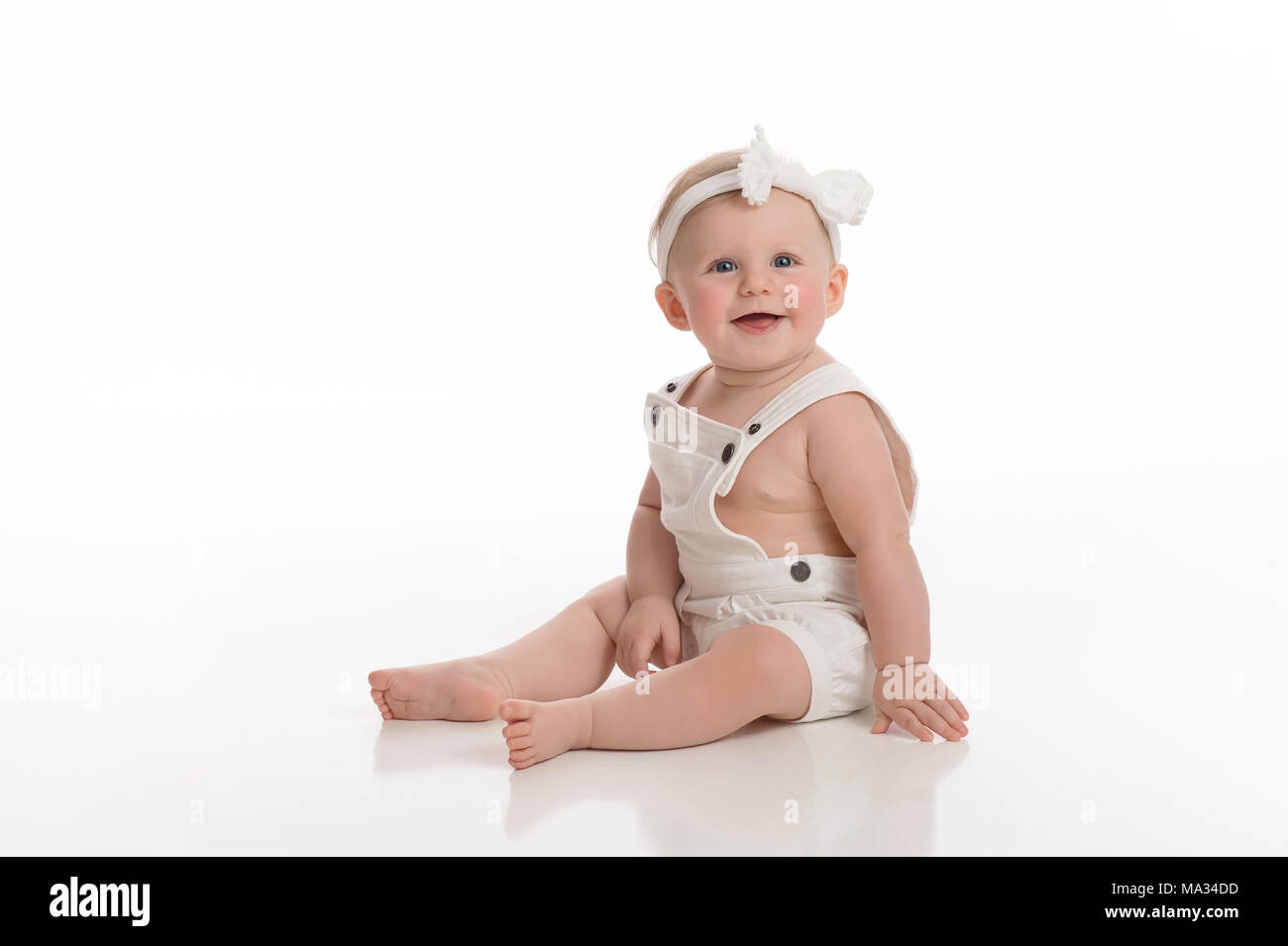 Una sonriente niña de siete meses monos vestidos de blanco. Rodada en el studio en un blanco, perfecto telón de fondo. Foto de stock
