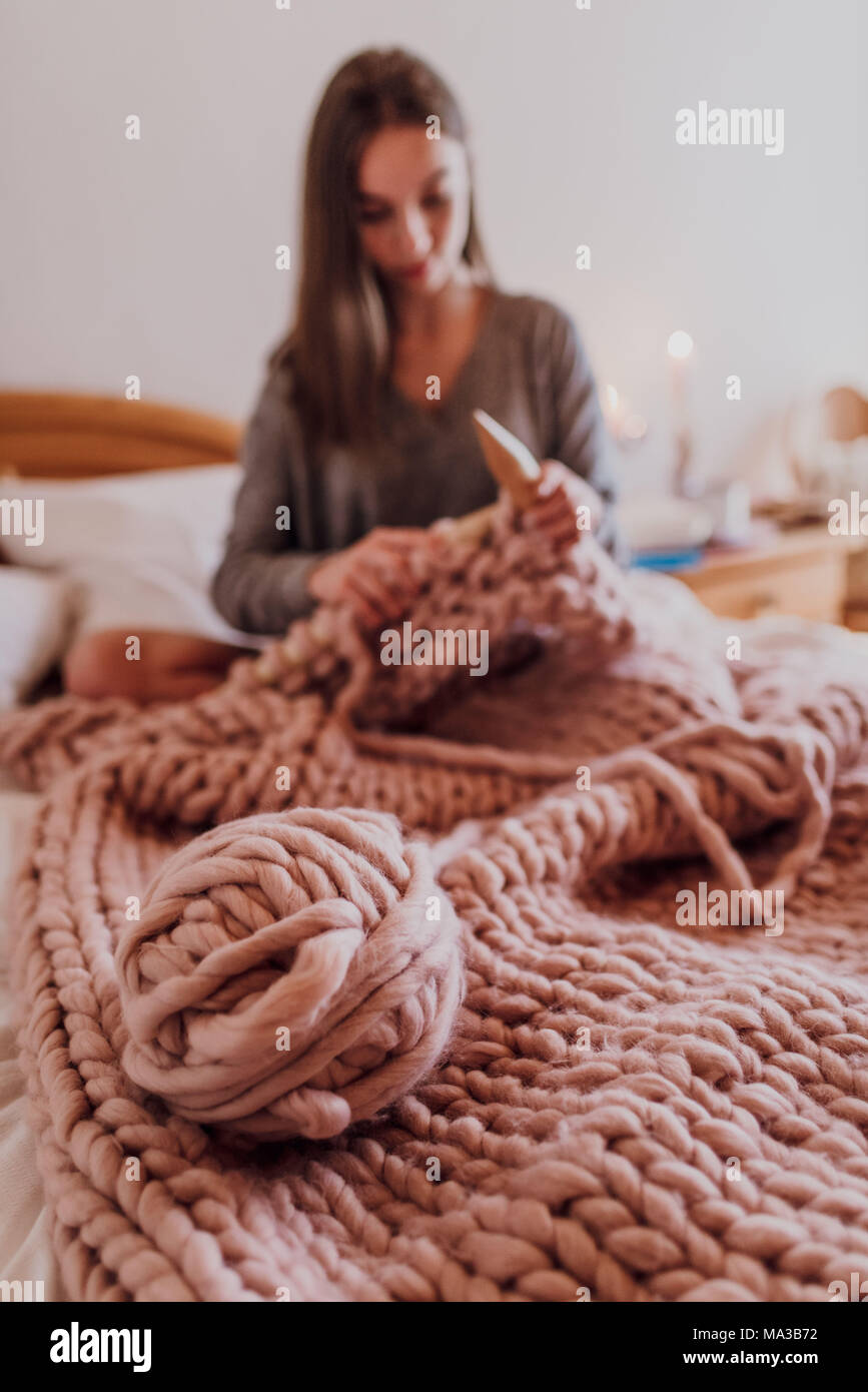Mujer joven sentada en la cama y tejido con lana XXL Foto de stock