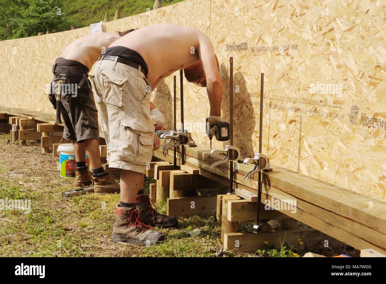 2 en una serie de 32, la construcción de una pasarela de madera. Los trabajadores corrección offset capas de madera con pegamento y tornillos en la forma de arco. Construcción de una SC Foto de stock