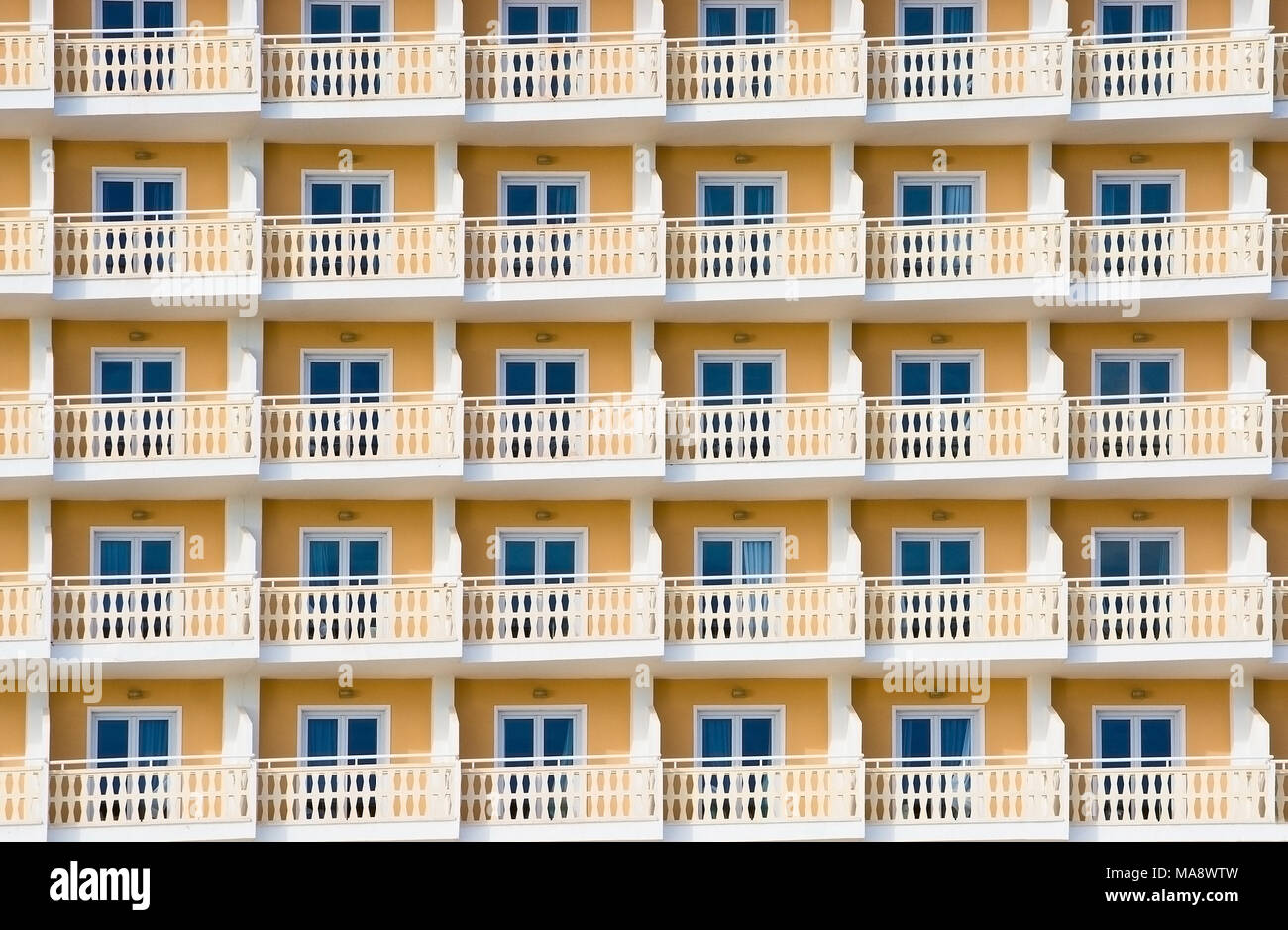 Hotel exterior amarillo con pequeños balcones y ventanas de fondo de turismo, España. Foto de stock