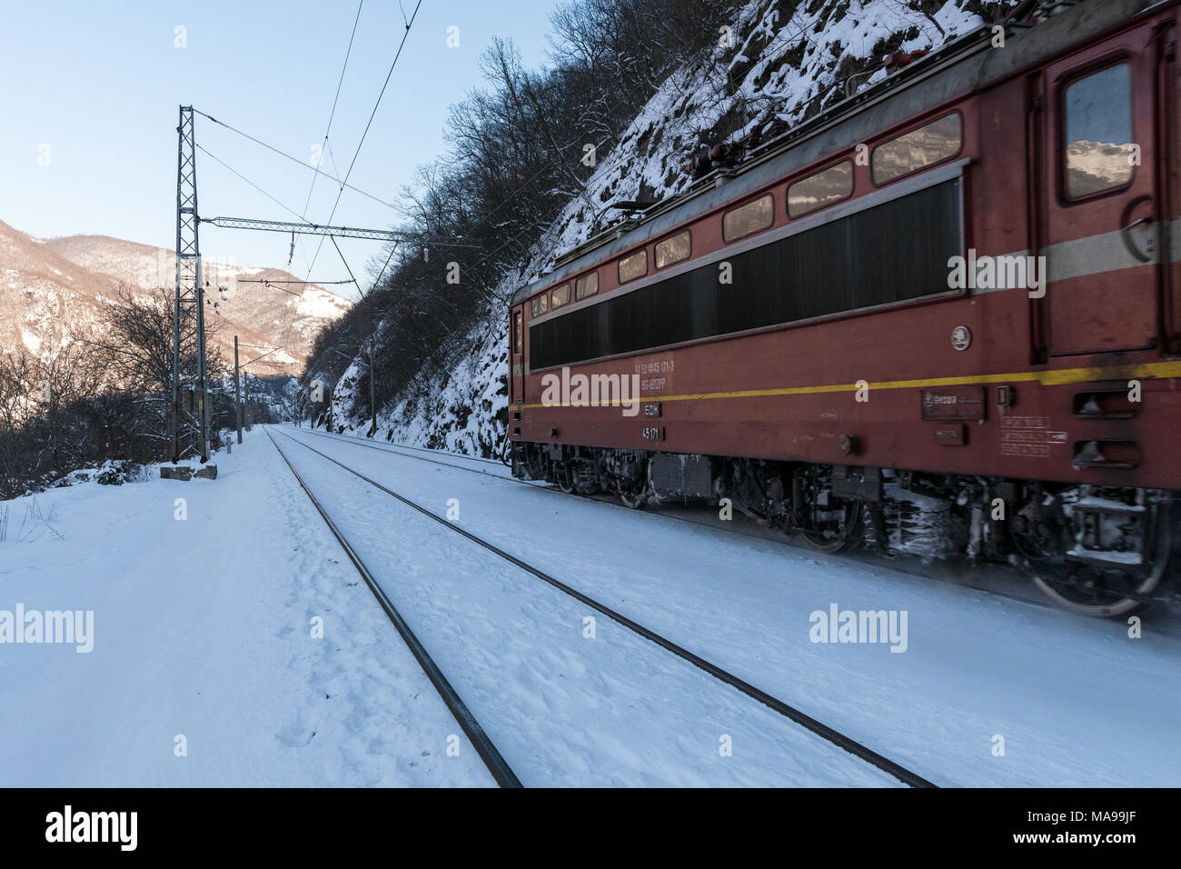 Locomotora eléctrica roja railway motor mueve en rieles cubiertos de nieve en Bulgaria durante el invierno Foto de stock