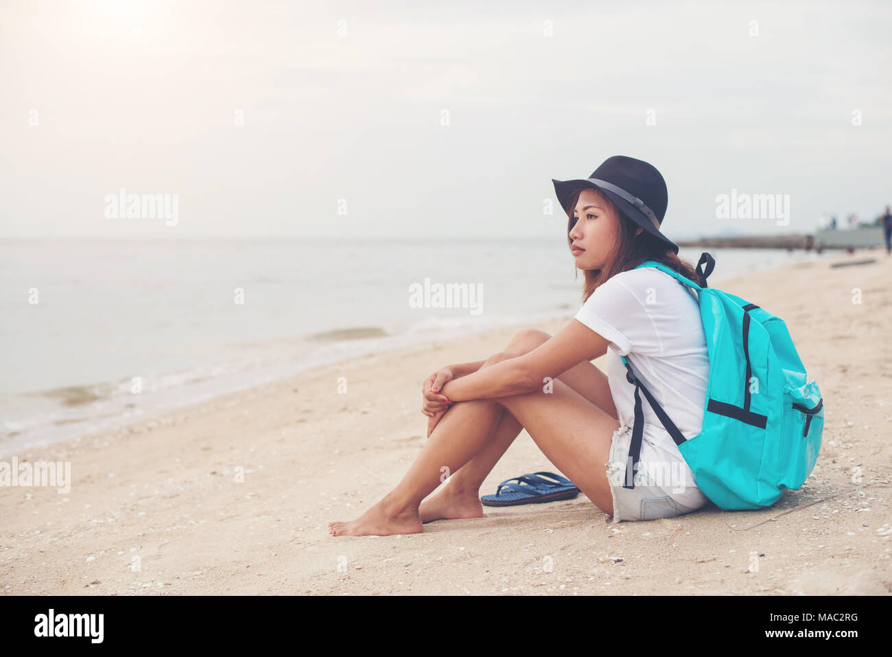 Mujer joven con mochila sentado en la playa solitaria y mirando en la  distancia Fotografía de stock - Alamy