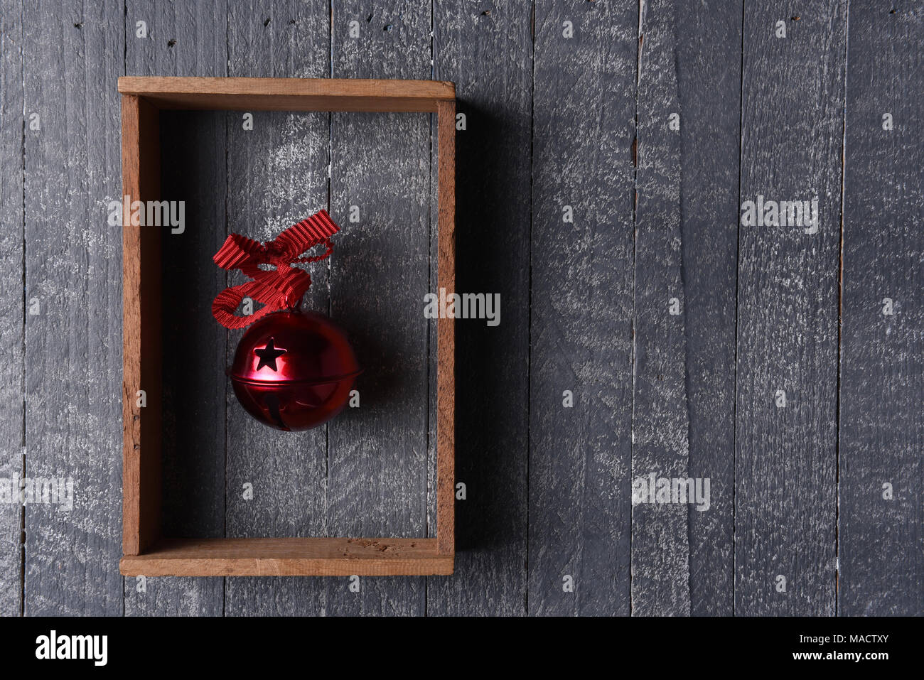 Un rojo jingle bell en un marco de madera en la pared de madera gris con espacio de copia. Foto de stock