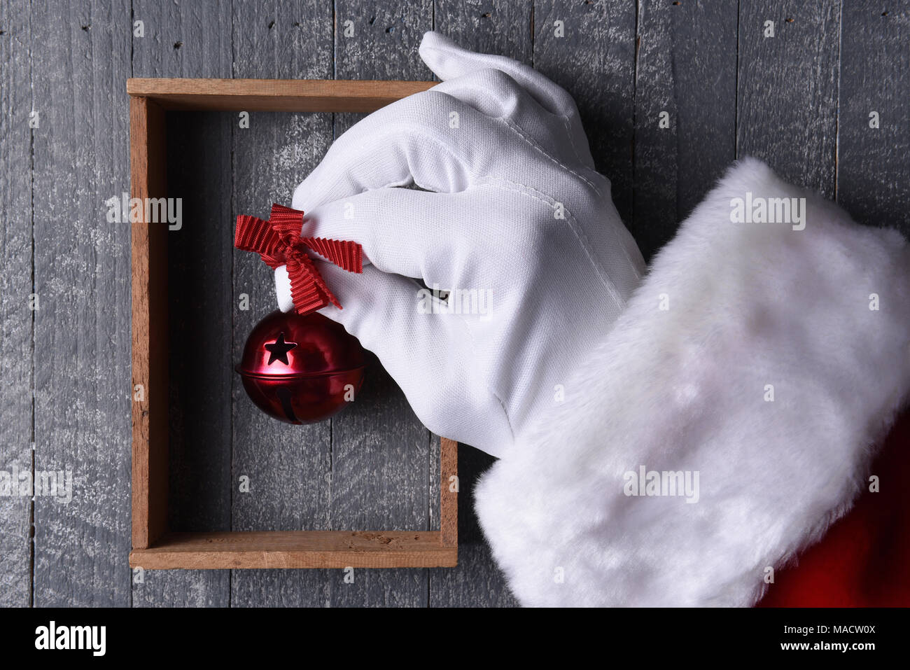 Santa Claus colgando un jingle bell rojo dentro de un marco de madera en la pared de madera gris. Foto de stock