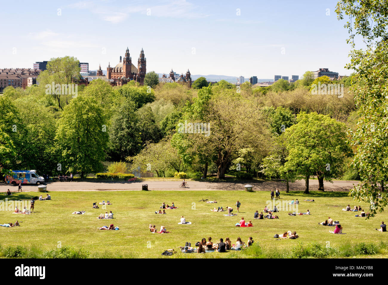 Los jóvenes, estudiantes de la Universidad de Glasgow, disfrutando de un cálido día de sol en el césped del parque Kelvingrove, Galería de Arte y Museo Kelvingrove en Foto de stock