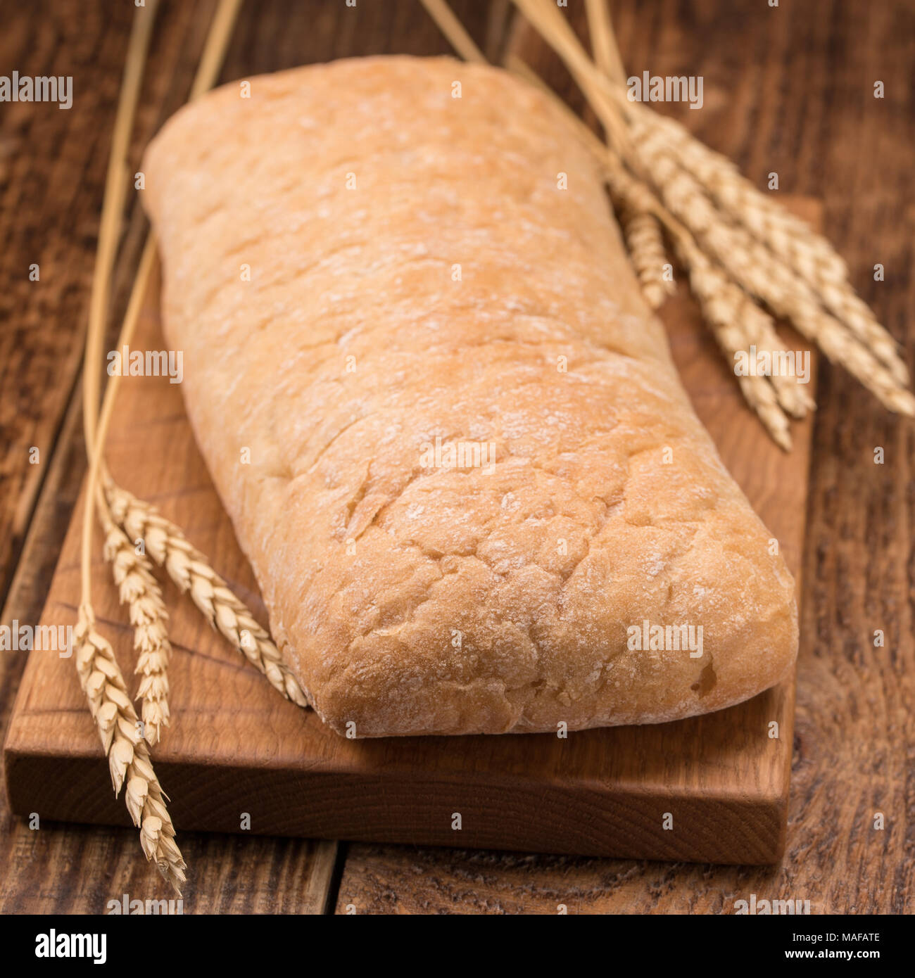 Sabroso pan casero fresco sobre una tabla de madera. Una monótona vida inmóvil con pan y spikelets de centeno. Una hogaza de pan sobre una tabla de madera. Foto de stock