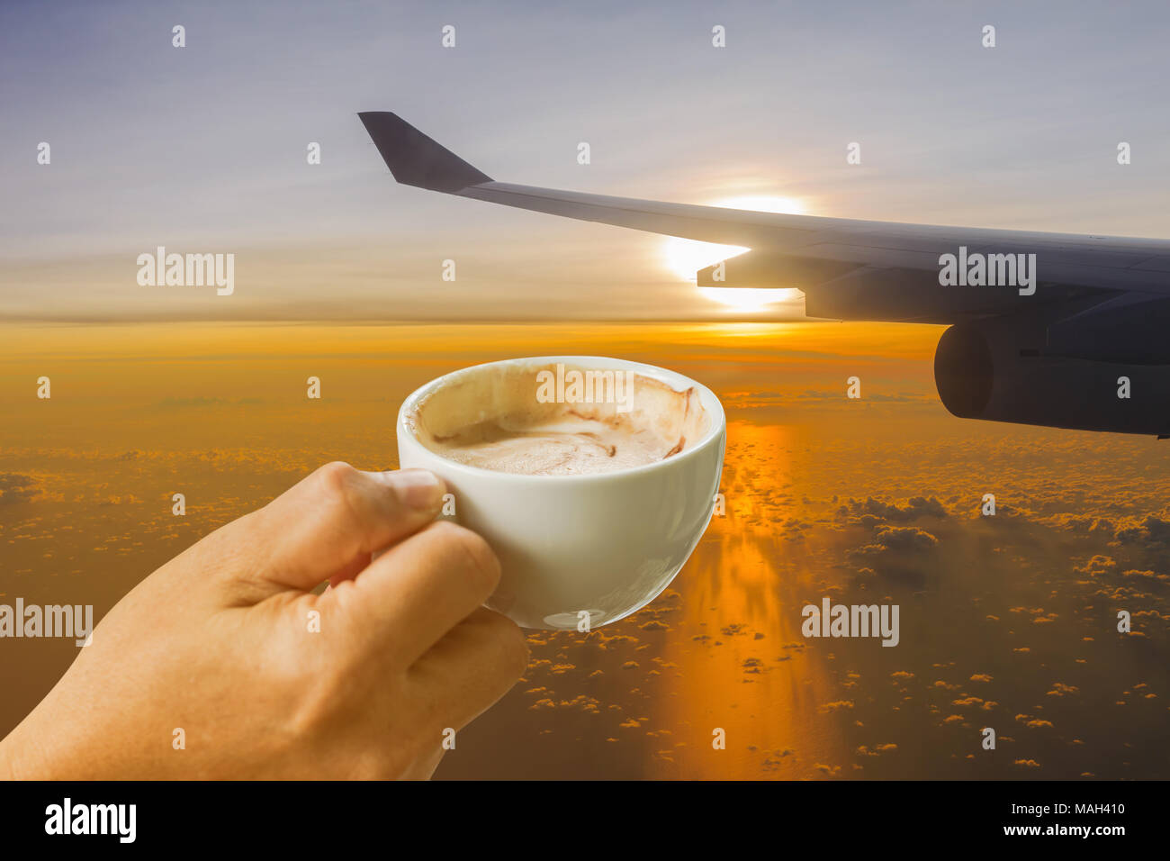 Taza de café en las manos de ala de avión contra la luz dorada del sol, temprano en la mañana antecedentes Foto de stock