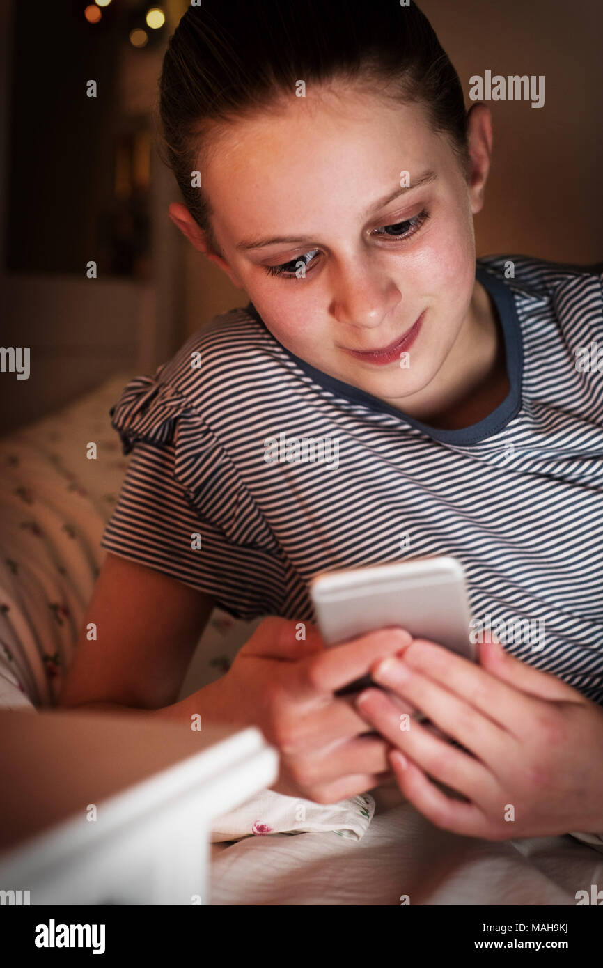 Joven Controlar mensajes de texto acostado en la cama durante la noche Foto de stock