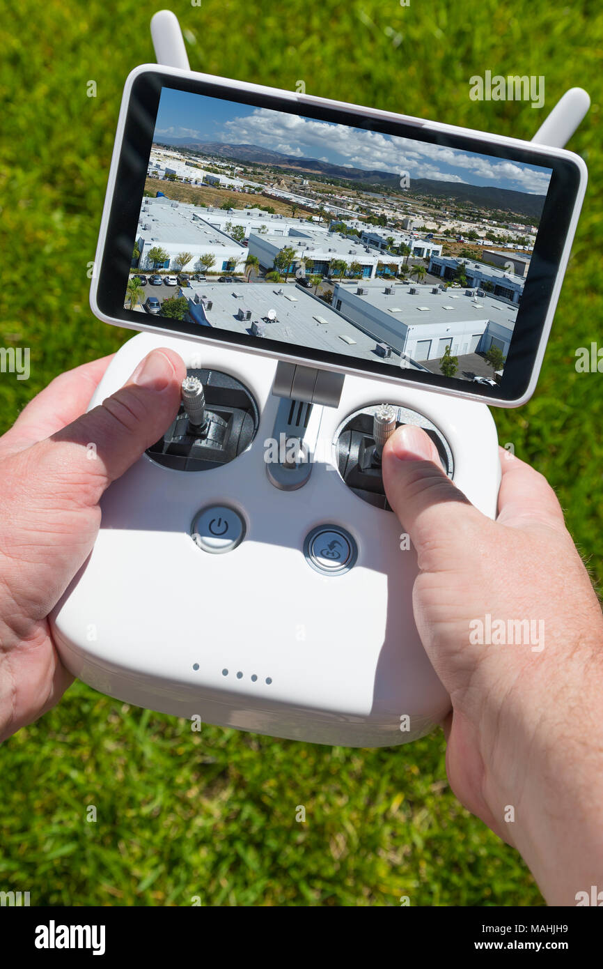 Manos sosteniendo Drone Quadcopter Controlador con edificios Indutrial en pantalla. Foto de stock