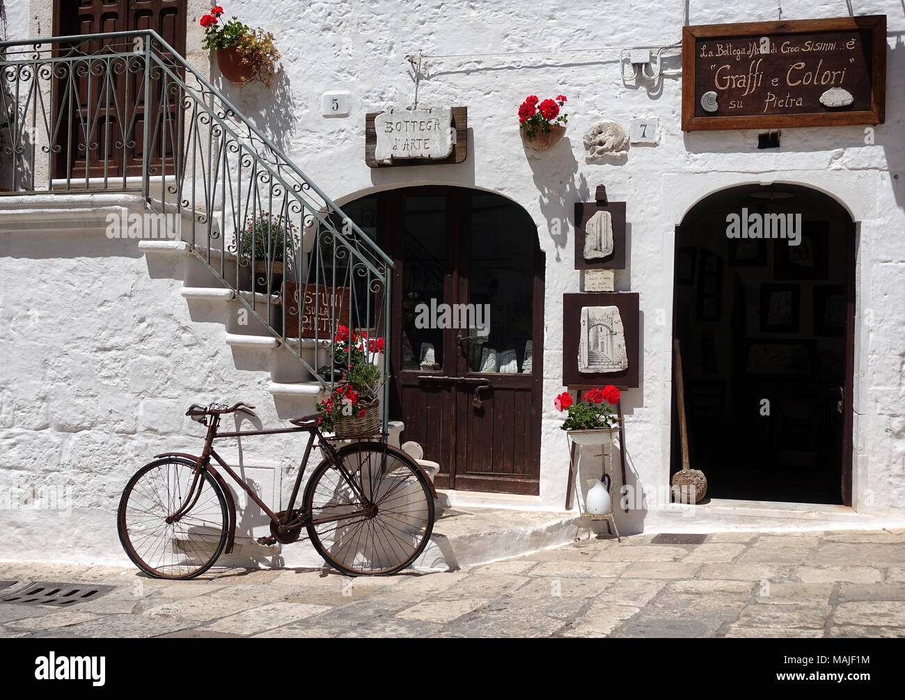Vieja bicicleta delante de una pared blanca con escaleras y puertas de madera marrón en un escaparate en la ciudad de Ostuni, Apulia, en el sur de Italia. Foto de stock