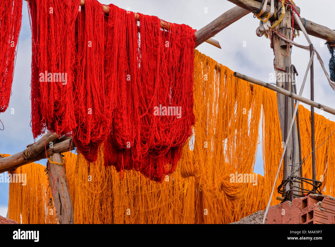 Marruecos Marrakech Medina Jemaa EL Fna zoco madejas de lana de lana teñidos de rojo y amarillo colgando de postes y secado al sol Foto de stock