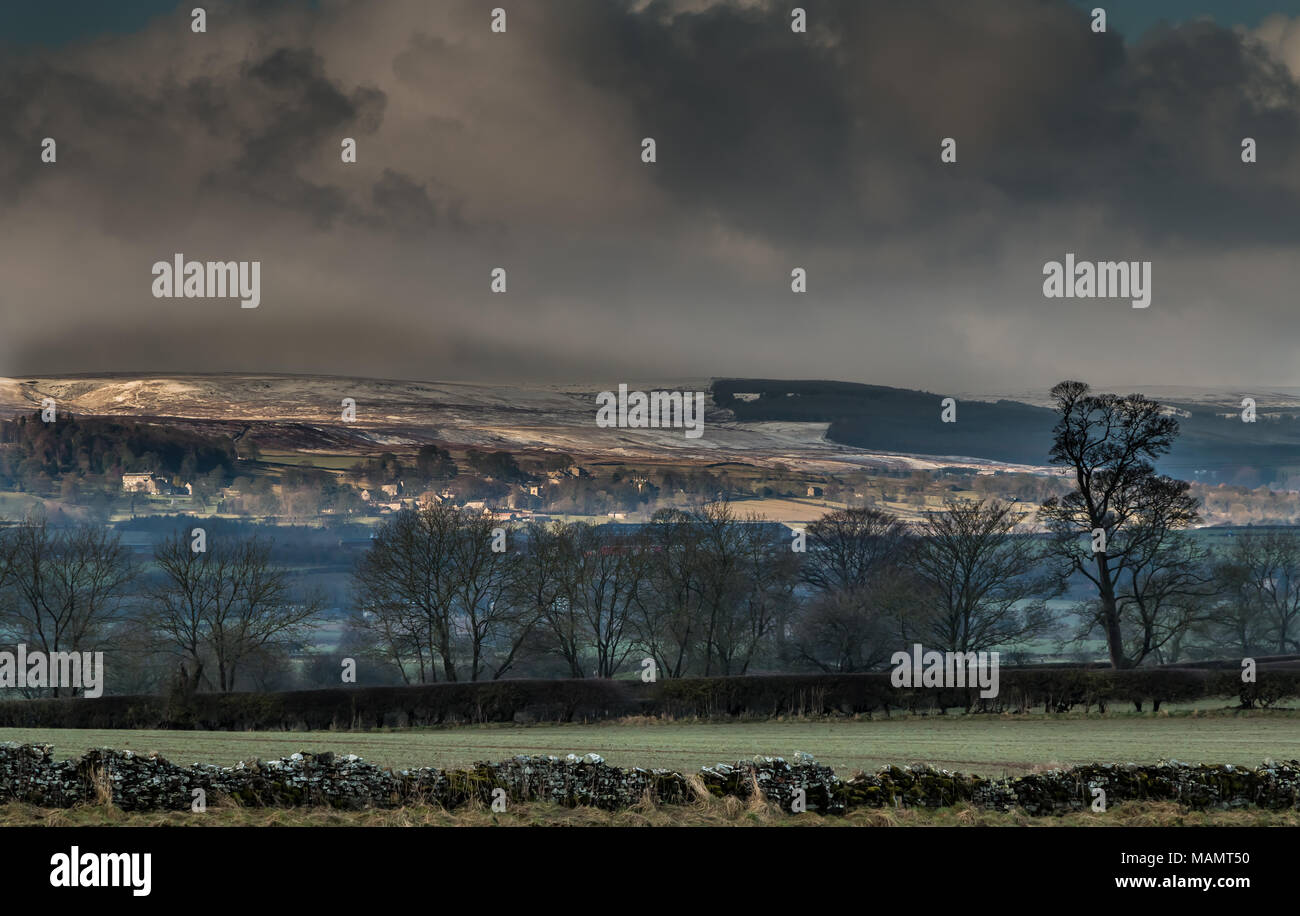 Paisaje de Teesdale, un breve intervalo soleado destaca la aldea de Barningham de conservación en zonas rurales, con una cubierta de nieve fresca en el páramo detrás Foto de stock