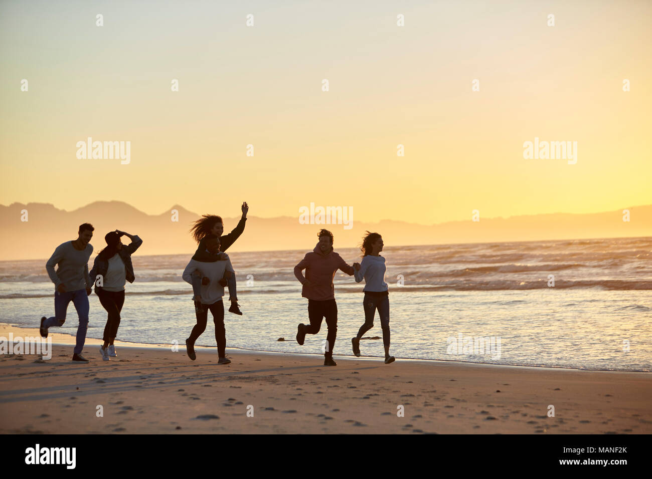 Silueta de amigos divirtiéndose en funcionamiento a lo largo de la playa de invierno Foto de stock