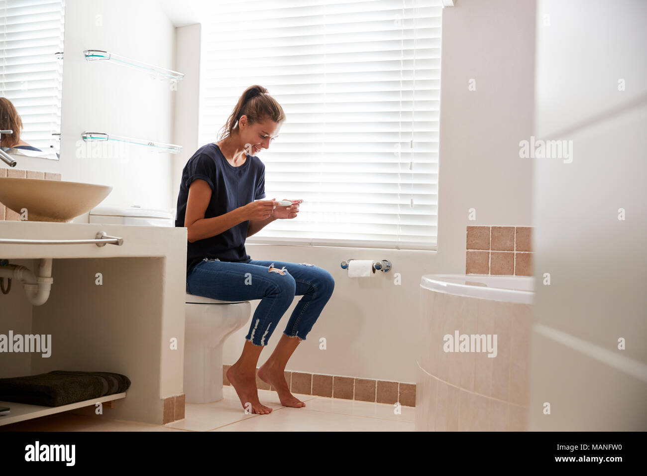 Mujer en el baño celebra el positivo resultado de la prueba de embarazo en casa Foto de stock
