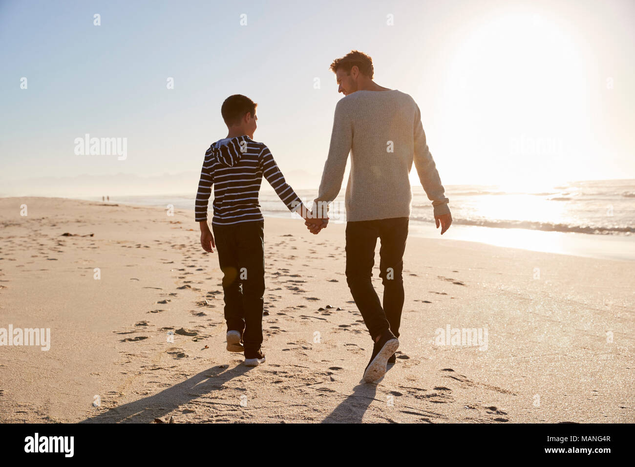 Vista trasera de padre e hijo, caminando por la playa de Invierno de la mano Foto de stock