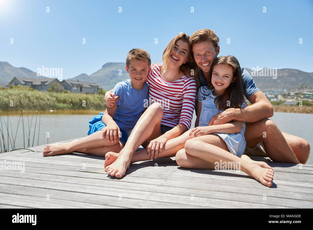 Retrato de familia sonriente sentado en el embarcadero de madera por el lago Foto de stock