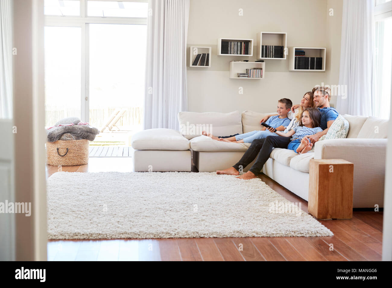 Familia sentada en un sofá en casa viendo la televisión juntos Foto de stock