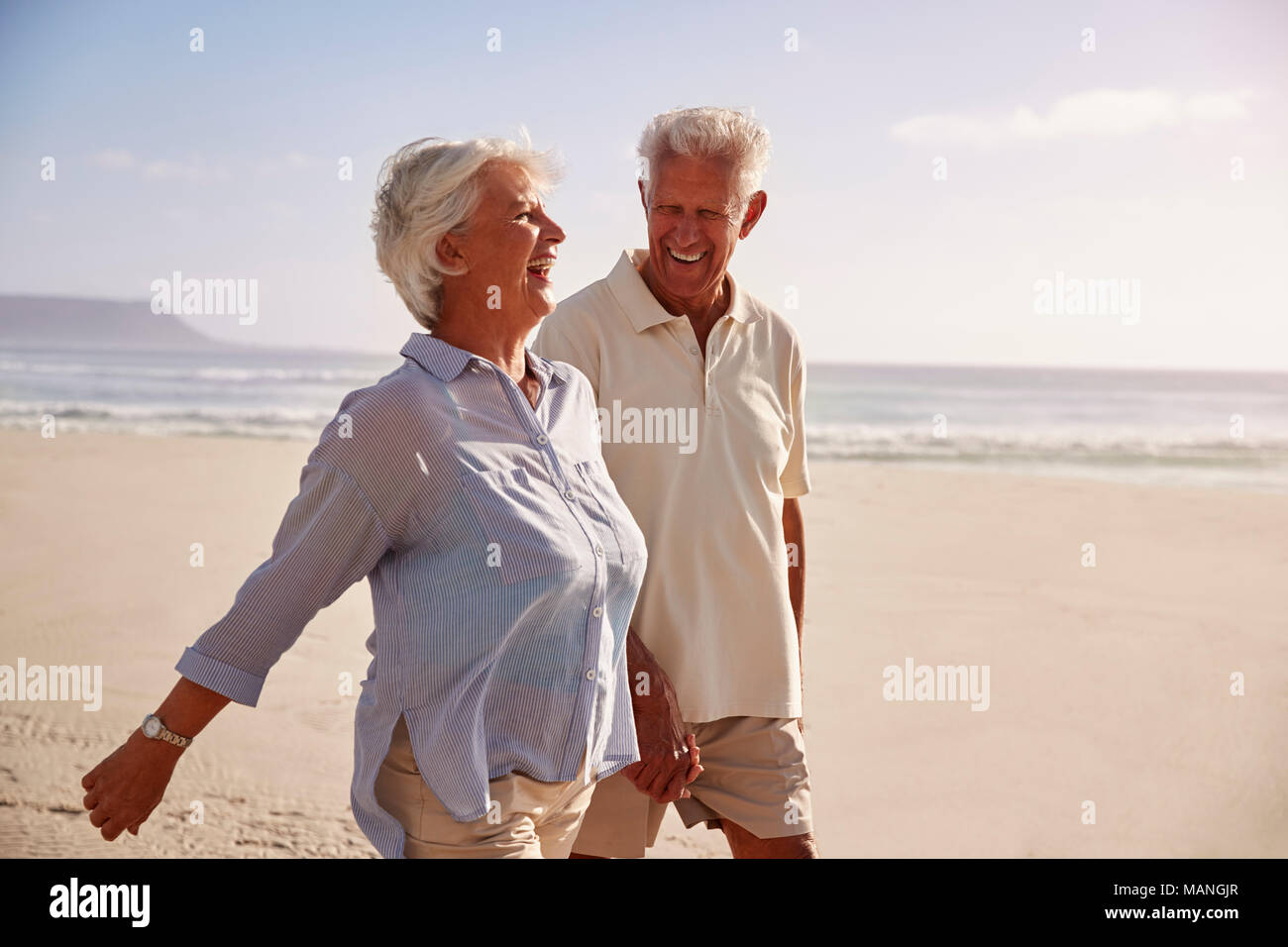Pareja de jubilados superiores a lo largo de la playa caminando juntos de la mano Foto de stock