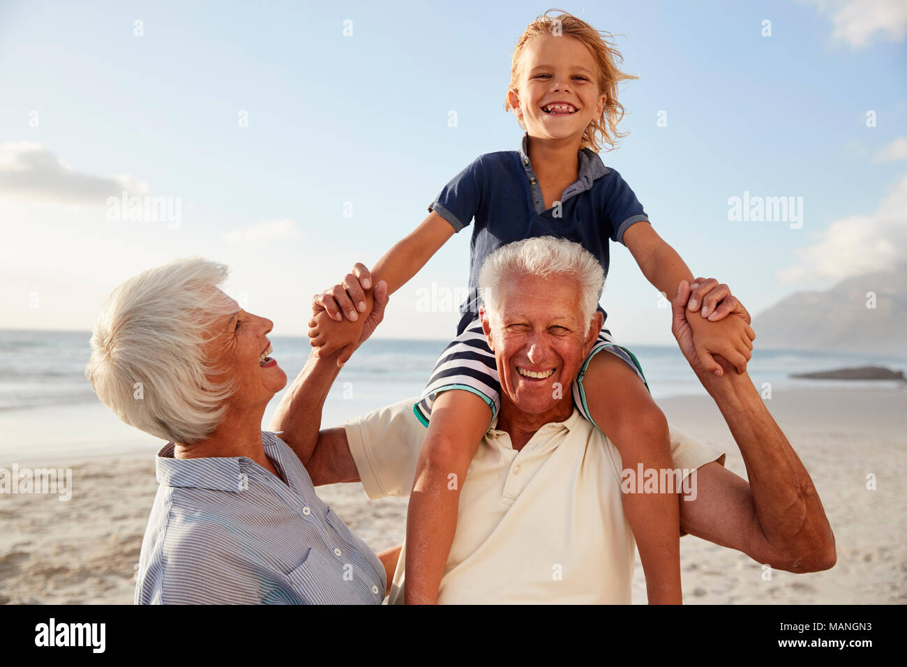 Los abuelos llevando a hombros nieto en caminar a lo largo de playa Foto de stock