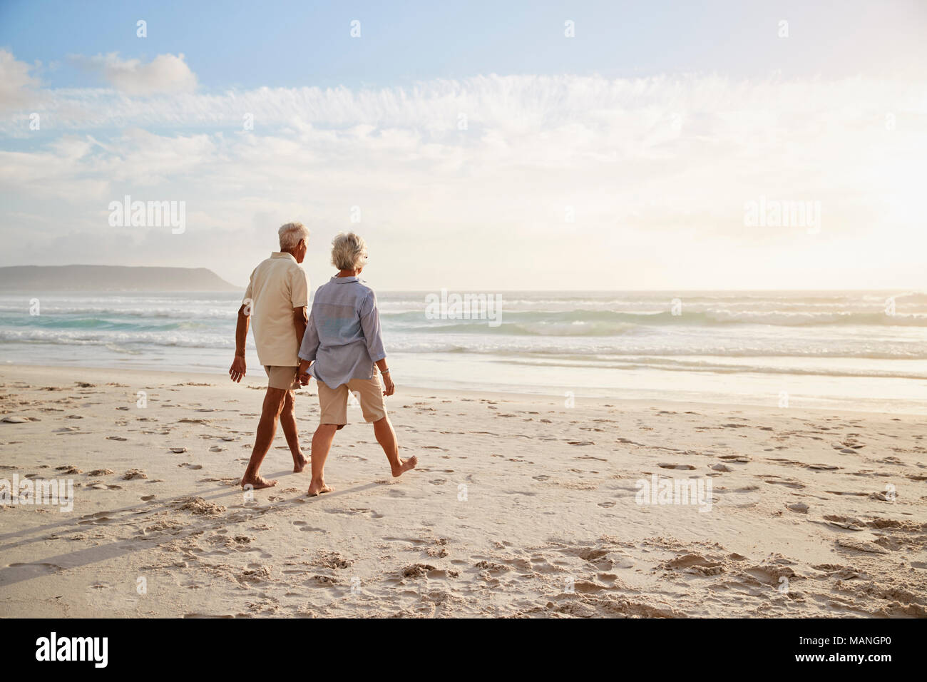 Vista trasera de las parejas ancianas caminando por la playa de la mano Foto de stock