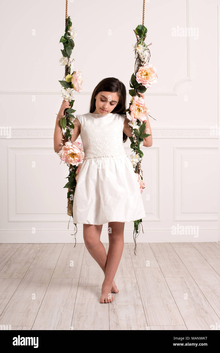 Niña vestidos de blanco vestido sentado en swing decorado con flores en la  luminosa y espaciosa habitación Fotografía de stock - Alamy