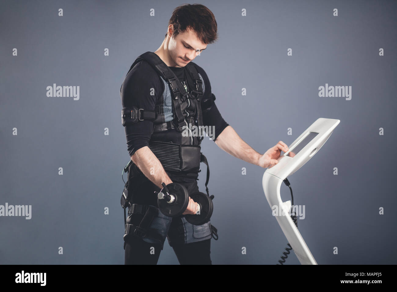 El hombre en traje de estimulación muscular eléctrica de pie con mancuernas  Fotografía de stock - Alamy