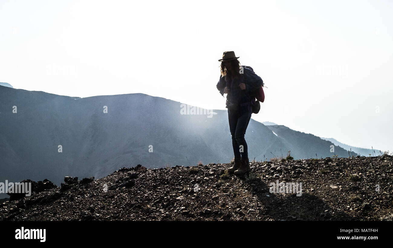 Excursionista hembra descansando después de subir una pendiente pronunciada en una zona montañosa agreste, humo de incendios en el fondo. (Las montañas costeras, BC, Canadá). Foto de stock