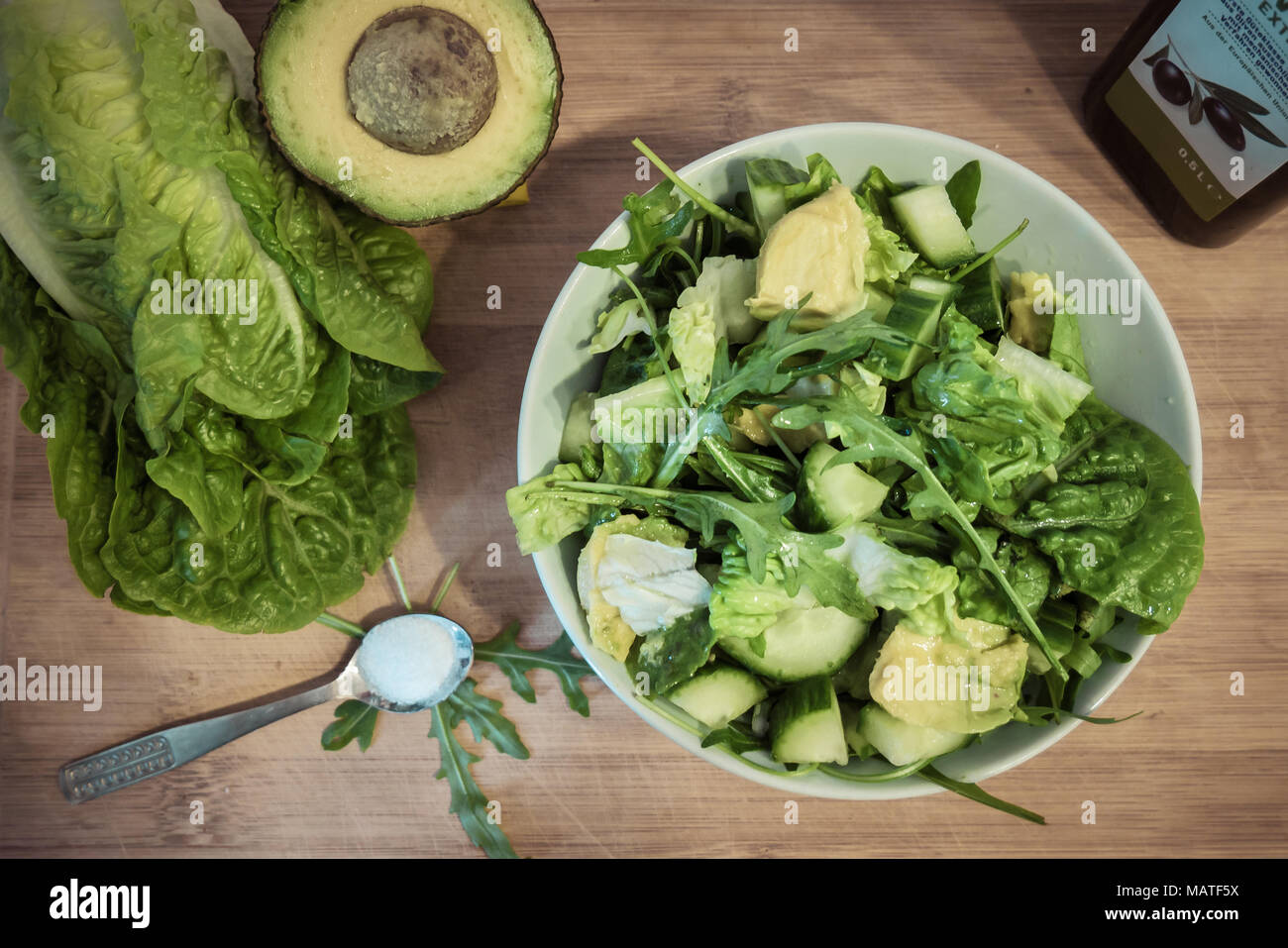 Alimentos saludables: una ensalada verde y los ingredientes (aguacate, sal, aceite de oliva, pepino y ensalada romana) sobre una tabla de madera. (Vista desde arriba) Foto de stock