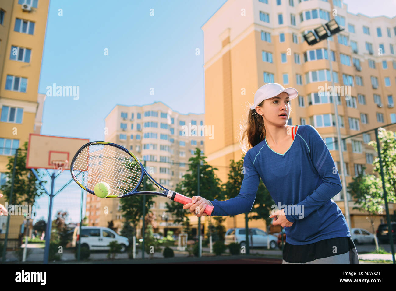 Mujer jugando al tenis al aire libre, Hot Shot ball. Practicar tenis en la pista de tenis en día soleado, sobre un fondo de ciudad Foto de stock