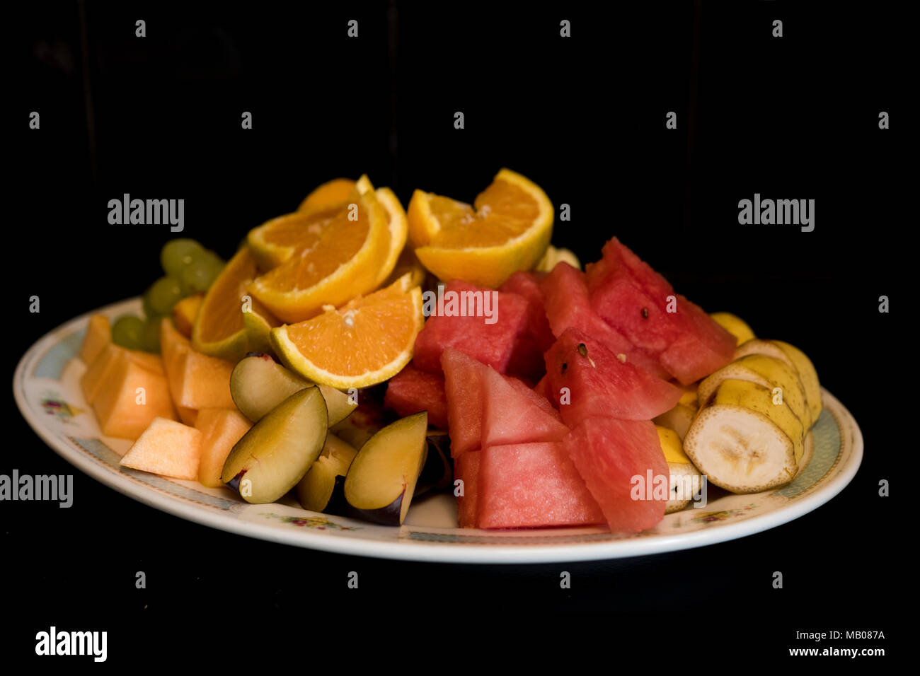 Un plato de frutas frescas cortadas sobre un fondo negro. Foto de stock