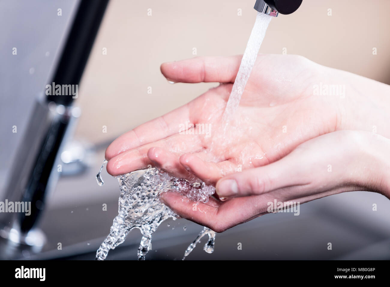 Mujer lava o lavando sus manos bajo el grifo de agua de un grifo en la cocina sobre un disipador de metal en una vista de primer plano Foto de stock