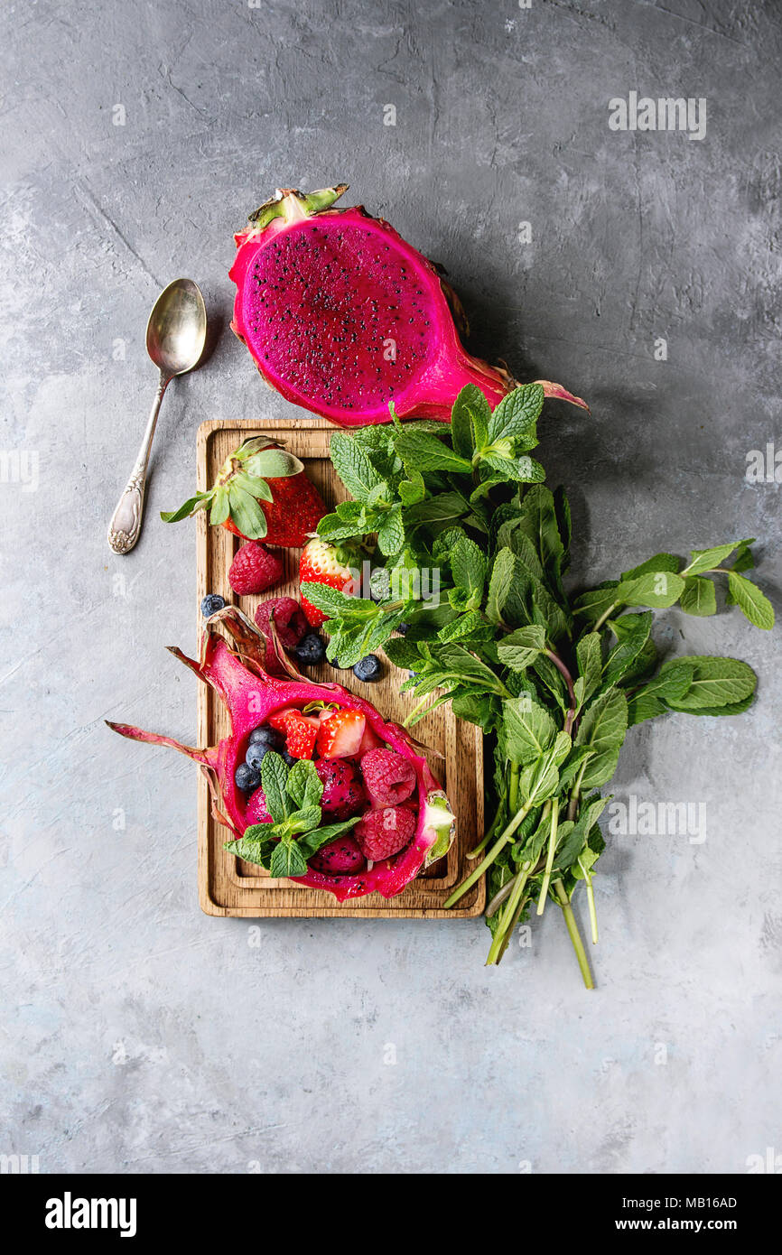 Vegan ensalada de frutas con fresas y menta en rosa dragon fruit con ingredientes por encima en madera sirviendo junta azul sobre fondo de textura. Principio V Foto de stock